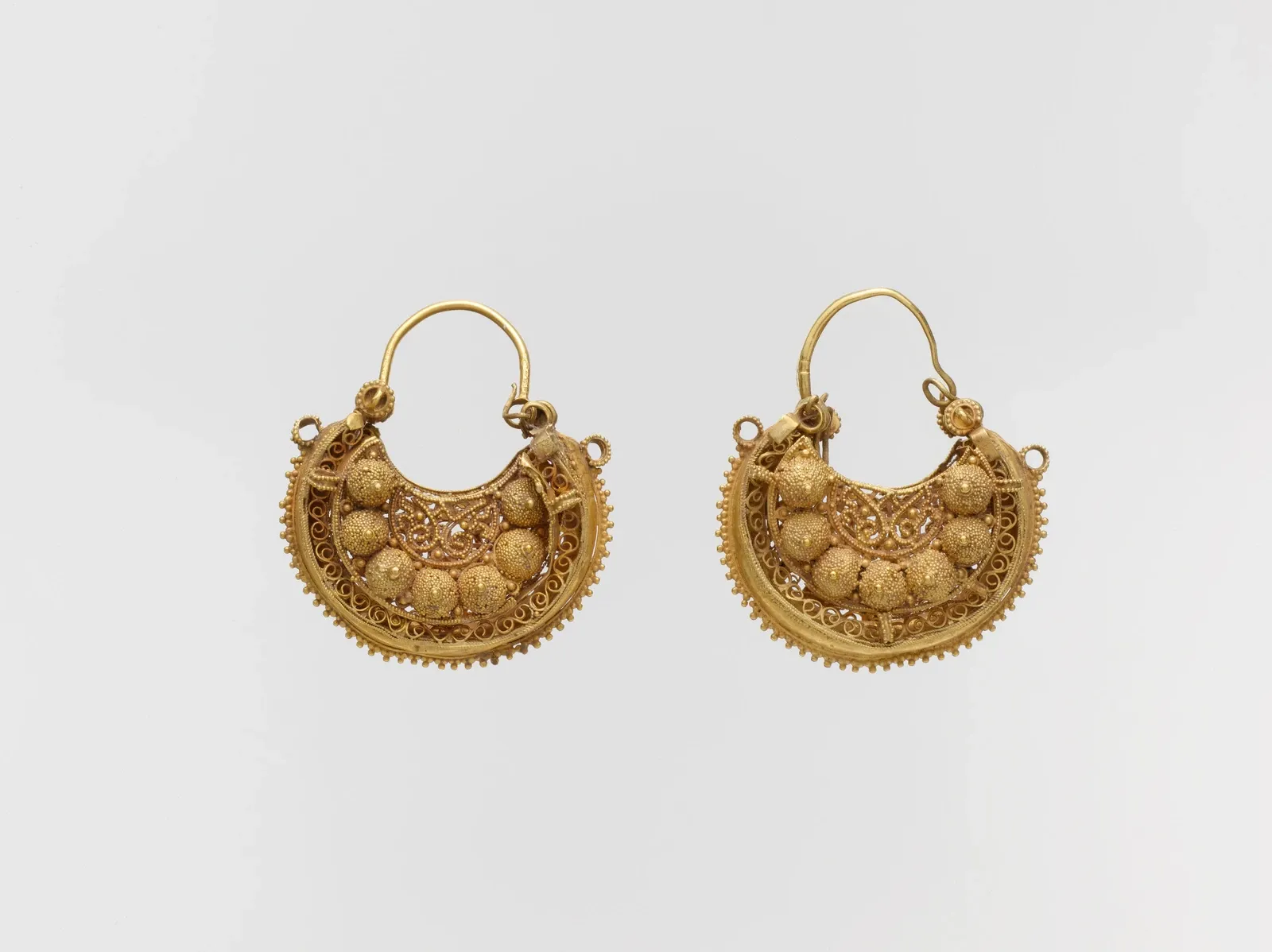 Two crescent-shaped gold earrings with delicate filigree and granulation