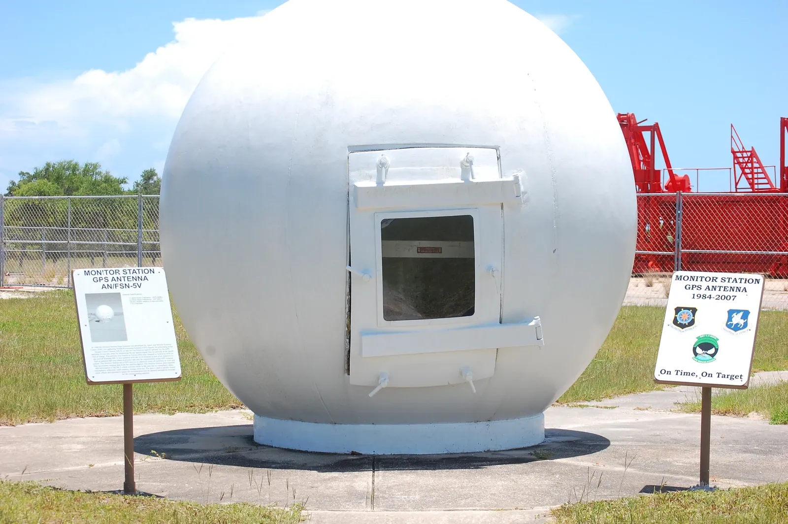 A white spherical radome from a retired GPS monitor station stands outdoors between two museum signs.