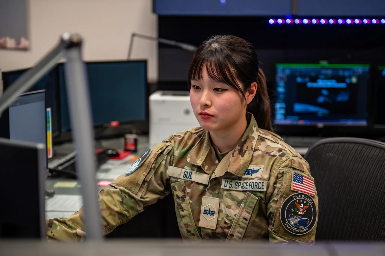 A Space Force satellite operator works at computer monitors in a control room.