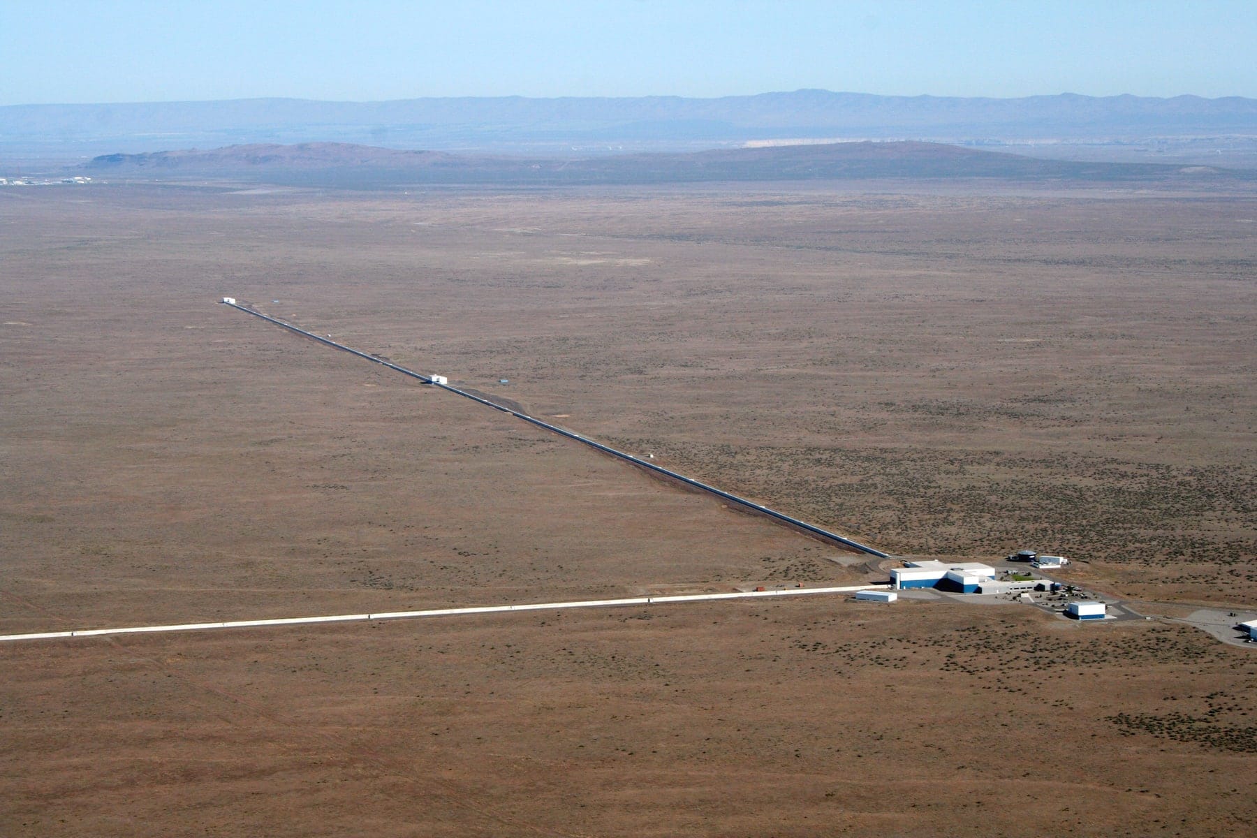 Aerial photograph of LIGO Hanford Observatory in Washington, showing the two perpendicular detector arms crossing a dry landscape.