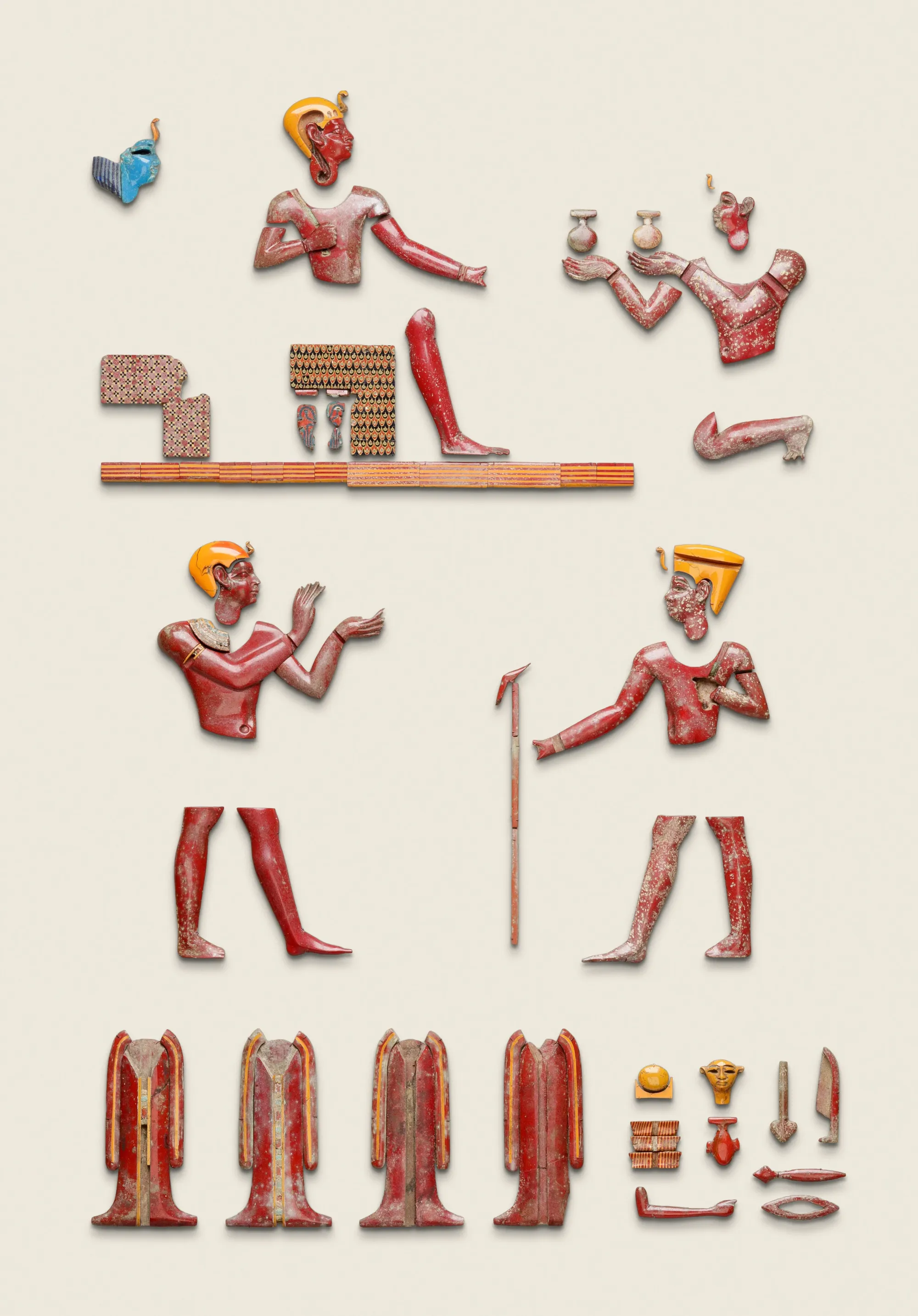 Museum arrangement of red, yellow and blue Egyptian glass inlays including figures and shrine fragments.