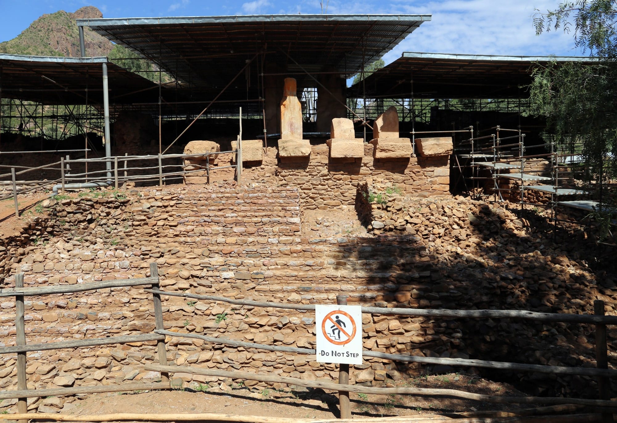 Stone podium and surviving entrance pillars at Grat Be’al Gibri beneath a protective shelter.