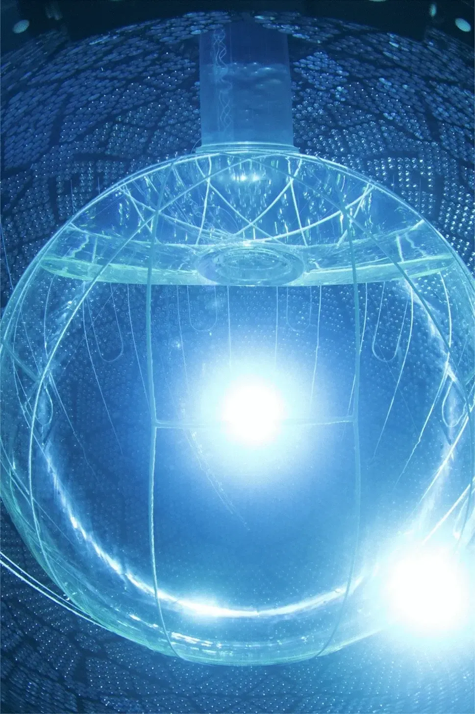 A transparent spherical detector vessel glows blue inside a surrounding array of light sensors.