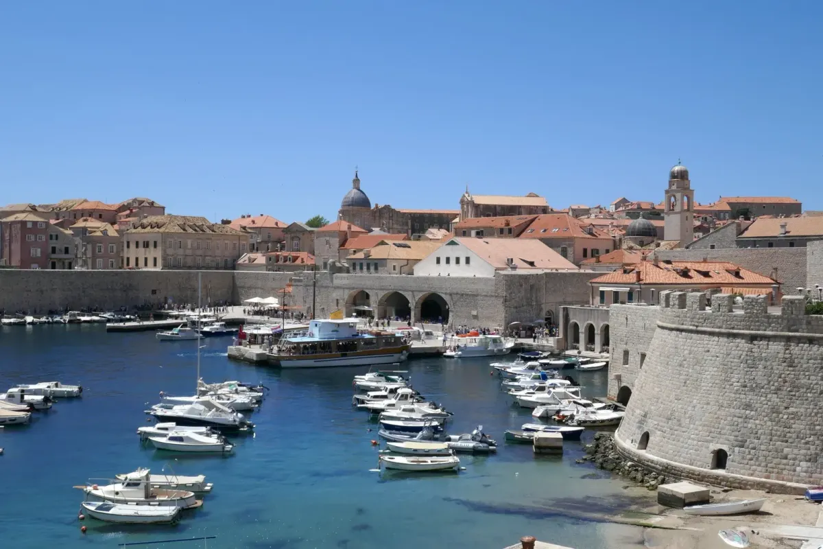 Dubrovnik’s Old Harbour in daylight, with boats, stone waterfront walls and the old city behind them.