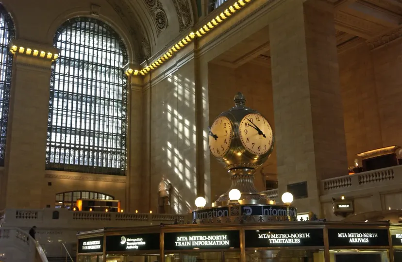 The four-faced clock in Grand Central Terminal under warm sunlight from a tall arched window