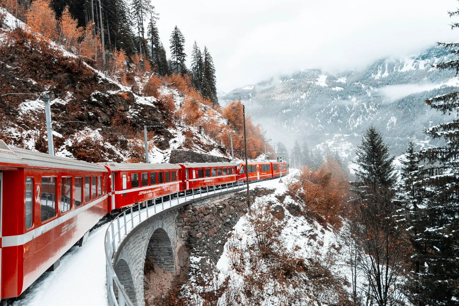 Scenic view of European train crossing snowy mountain landscape in winter, surrounded by forests, Switzerland