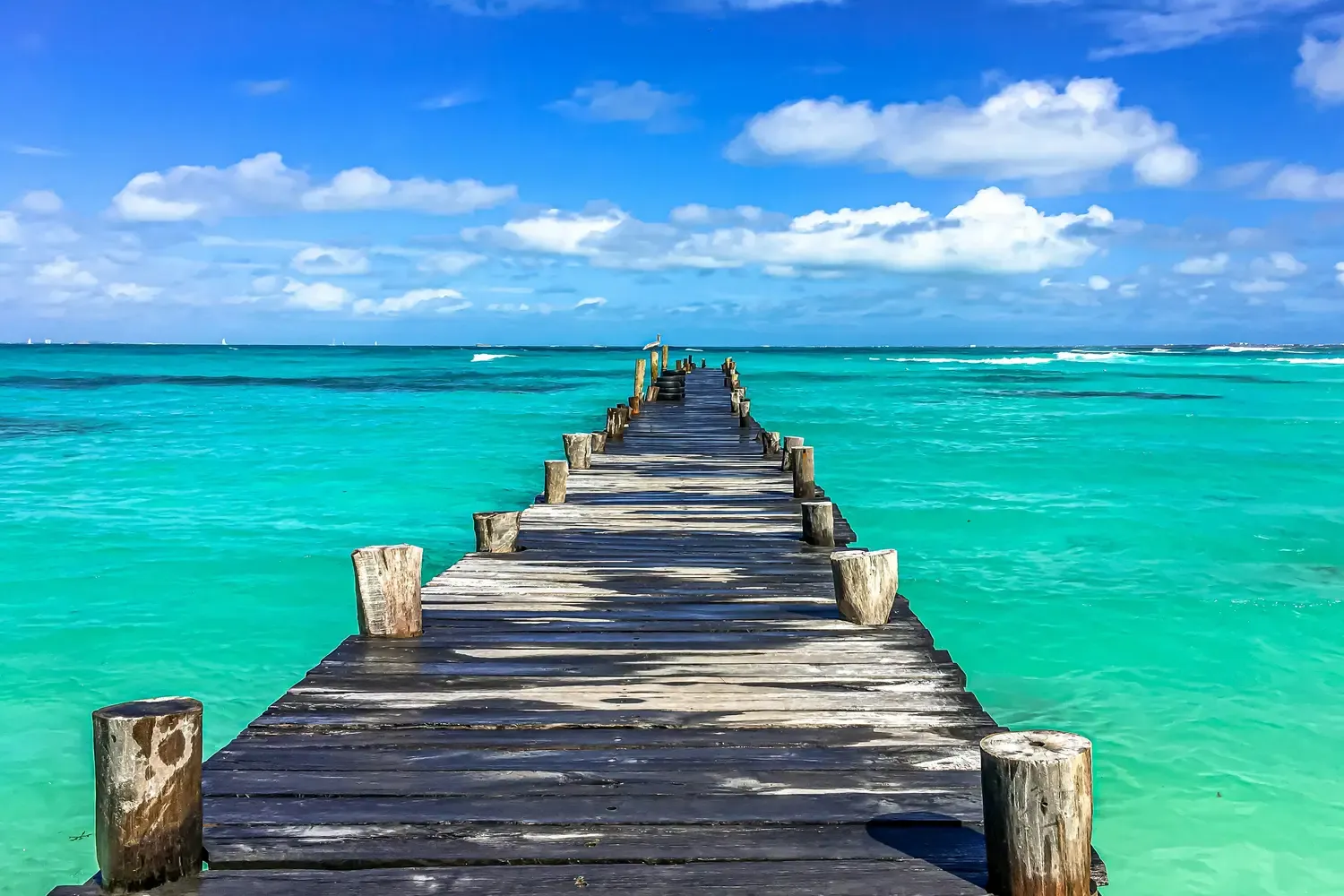 Wooden pier extending into turquoise Caribbean water under a blue sky