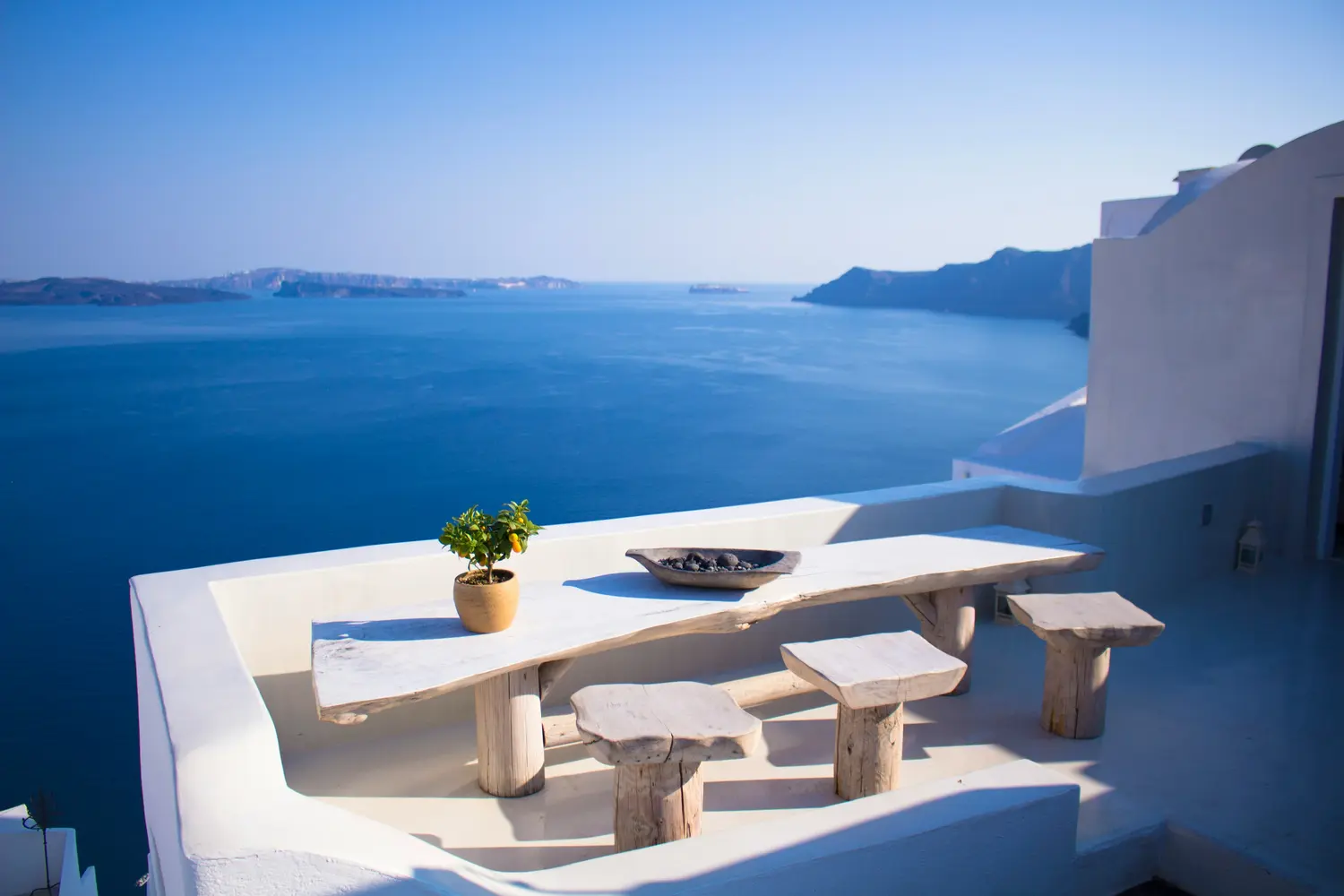 rustic stone dining set with a live-edge table and matching log stools on a white terrace overlooking the blue sea in Santorini, Greece.