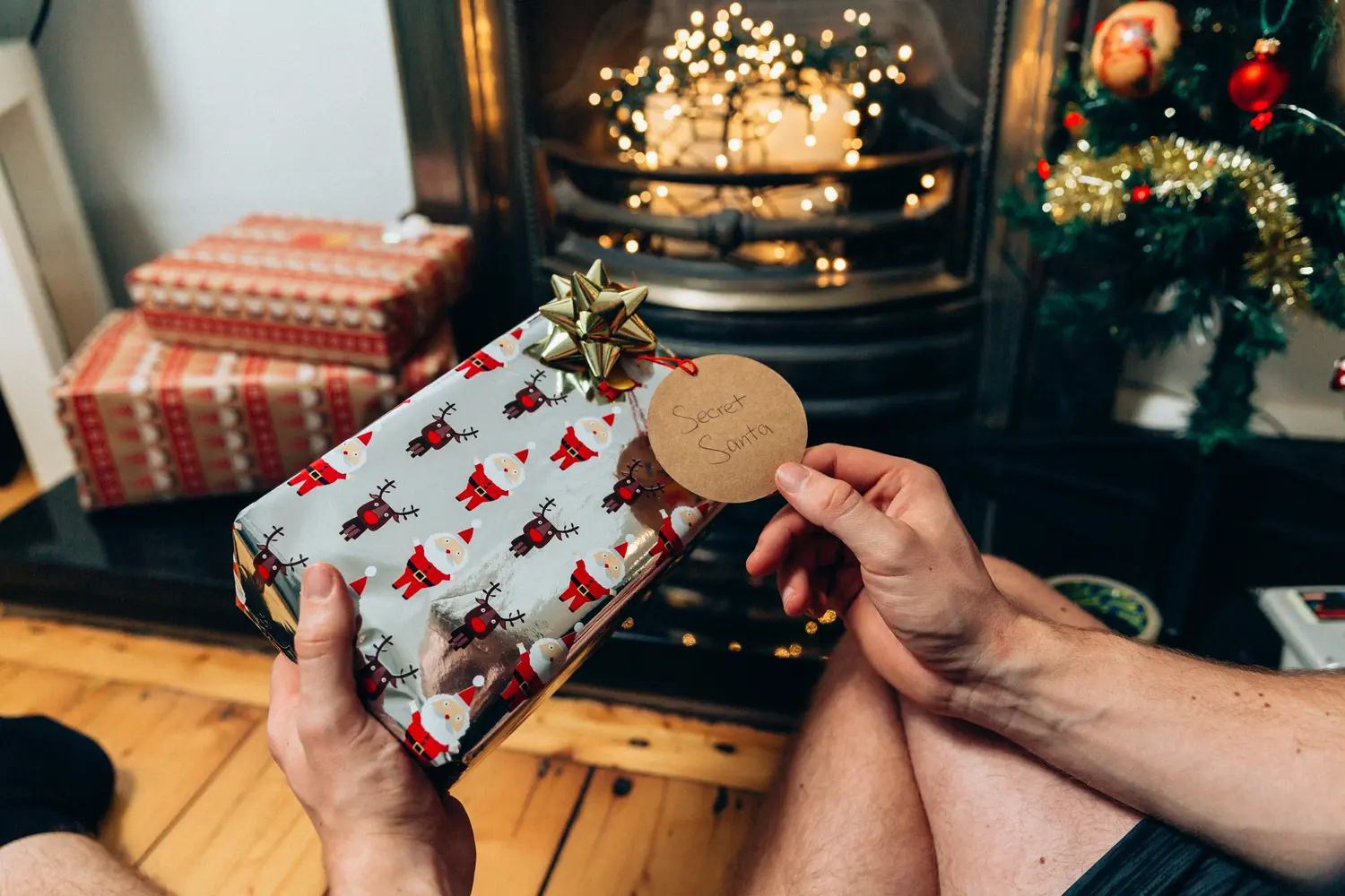 A person holding a Christmas present wrapped in Santa-patterned paper