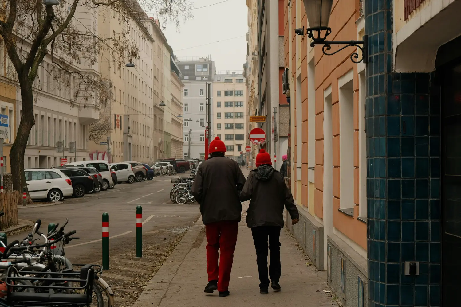 Two people in red winter hats walking down a sidewalk on a city street in Vienna, Austria