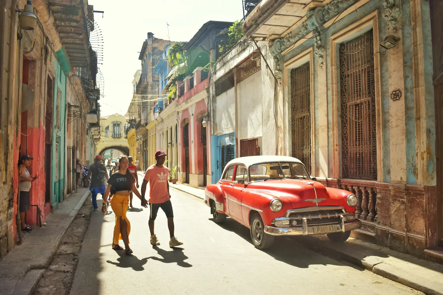 Colorful historic street in Havana with pedestrians and a vintage red car.