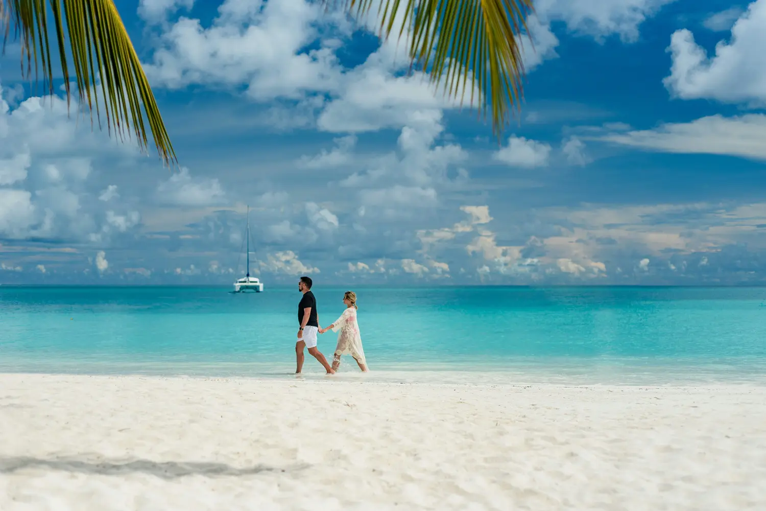 A couple walking on a white sand beach with turquoise water
