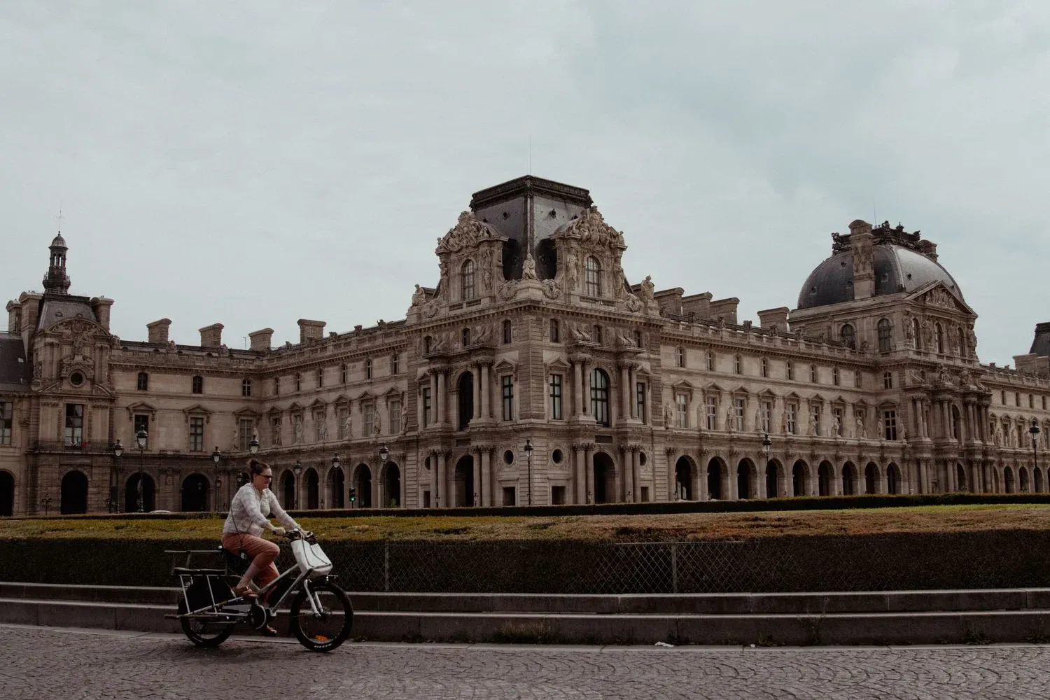 A person cycles past the famous Louvre Museum in Paris