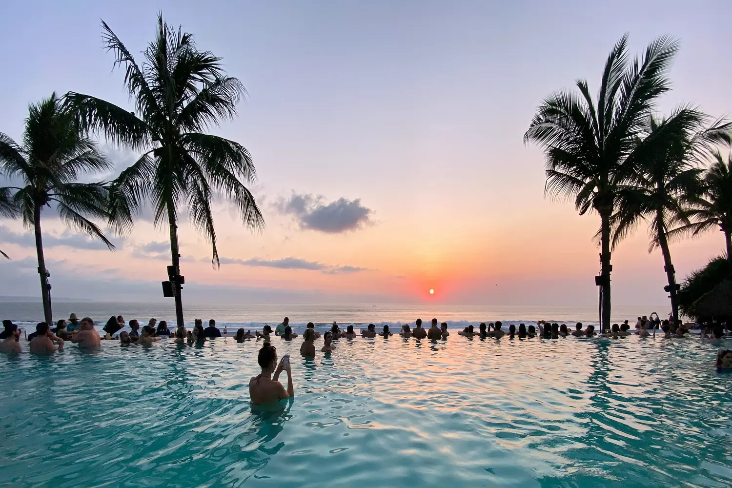 People enjoying the sunset from an infinity pool overlooking the ocean at the Potato Head Beach Club in Seminyak, Bali, Indonesia