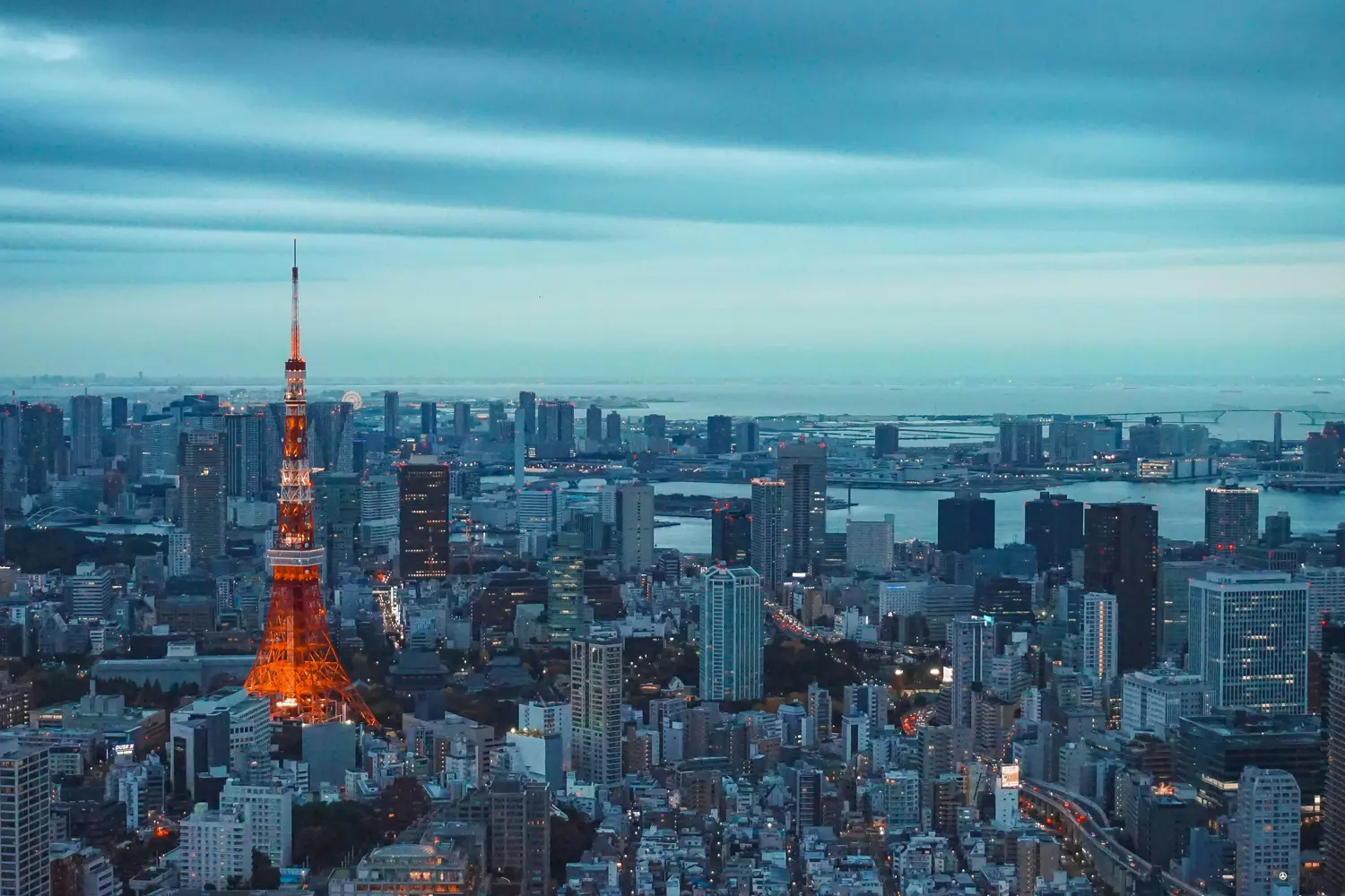 lluminated orange and white Tokyo Tower standing amidst the dense urban skyline of Minato Ward, Tokyo, Japan