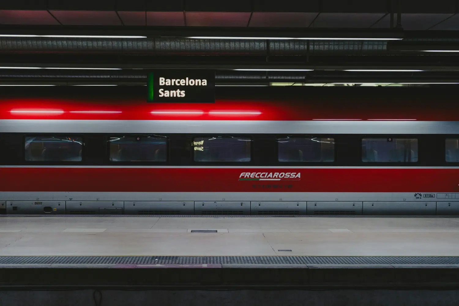Red and silver Frecciarossa high-speed train with an overhead sign reading Barcelona Sants in Barcelona, Spain