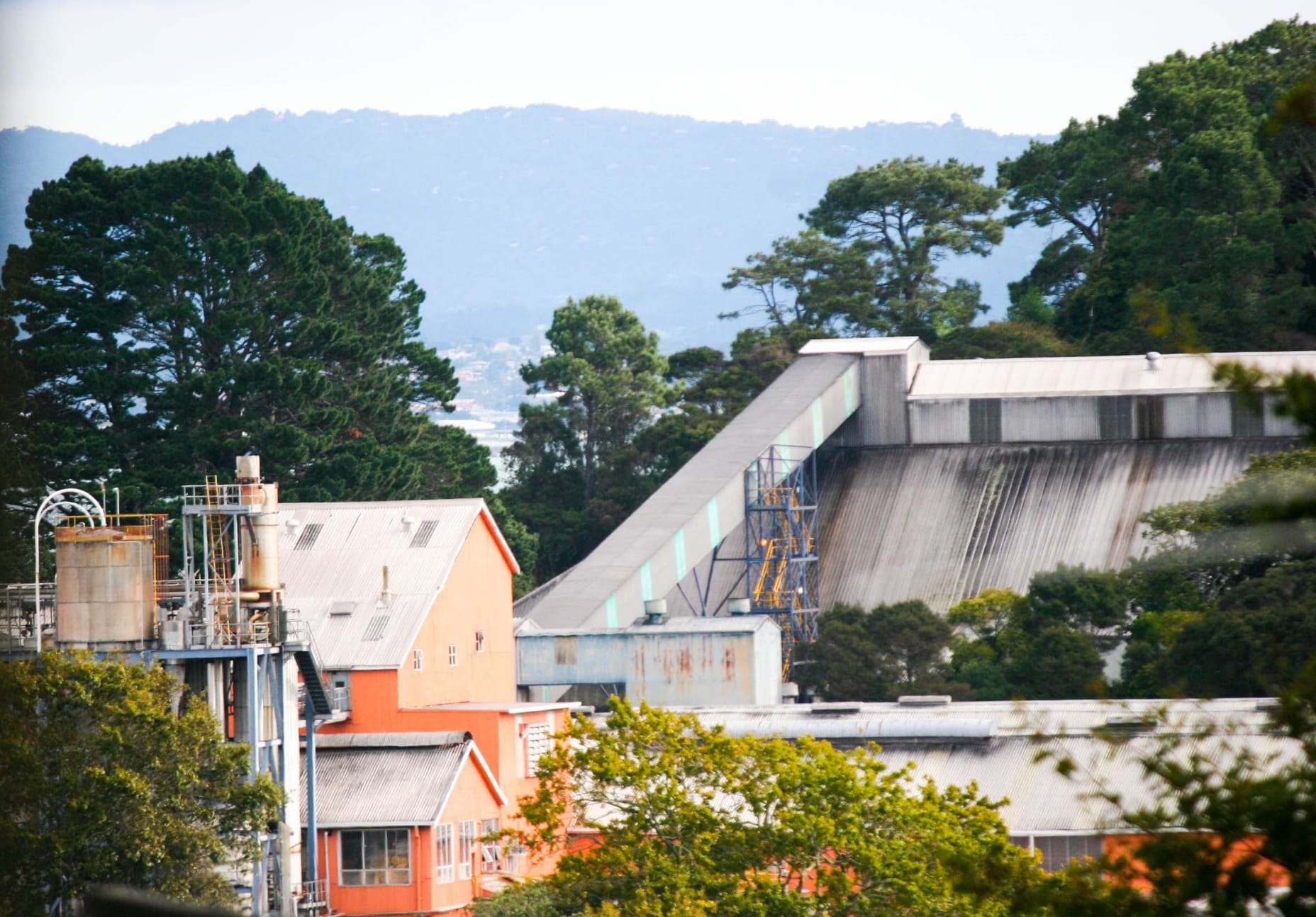 A factory nestled in a forest with hills in the background