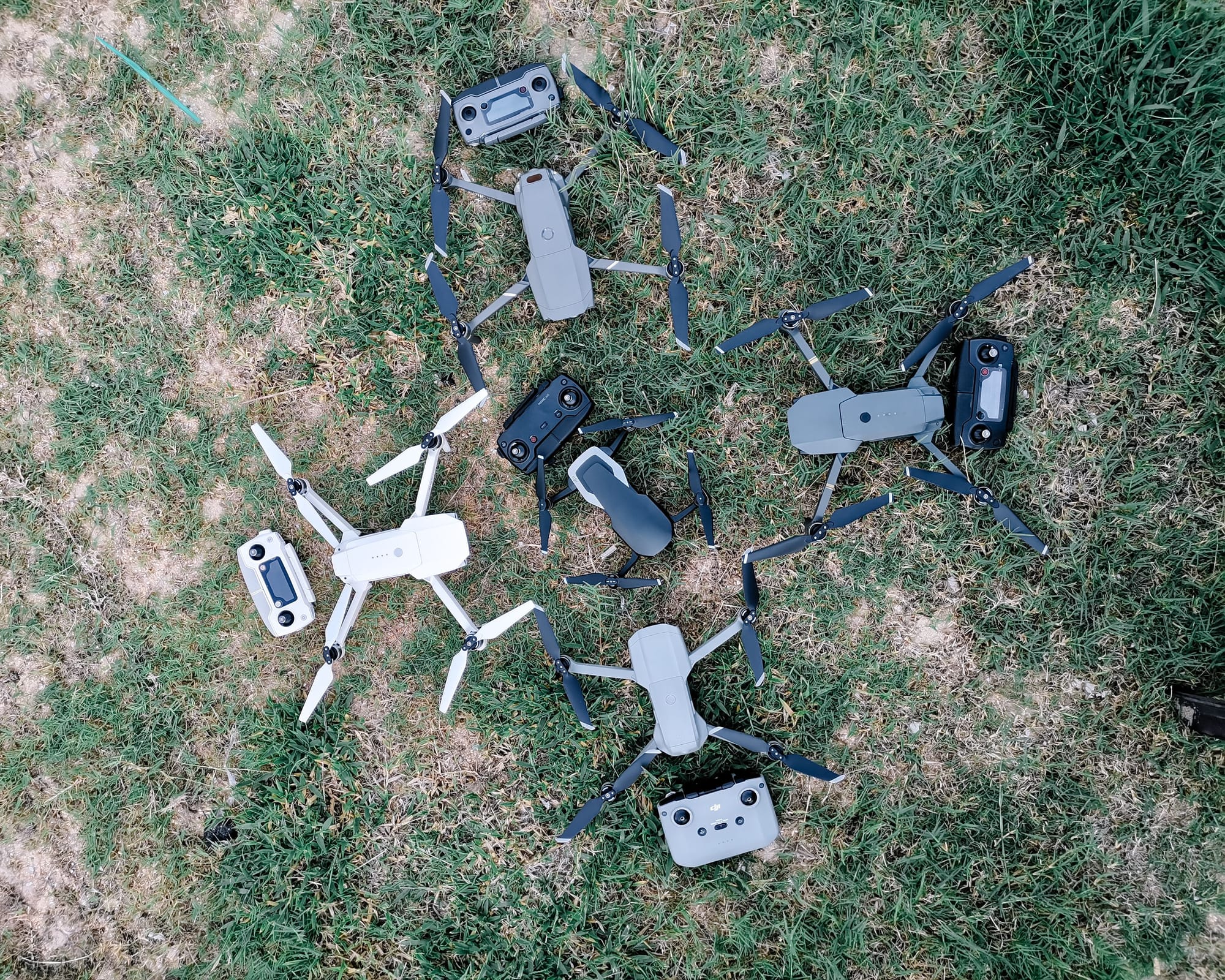Assorted drones and controllers arranged on a grassy terrain viewed from above by Pok&nbsp;Rie