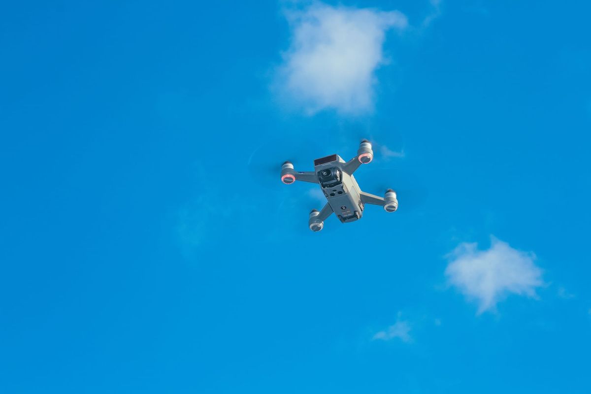 Aerial view of a drone cruising in a bright blue sky with scattered clouds by Pok Rie