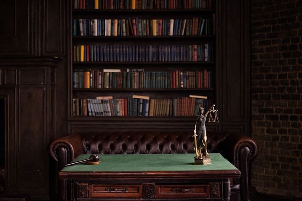 A classic study room with shelves of books, a gavel, and Lady Justice figurine on a green table