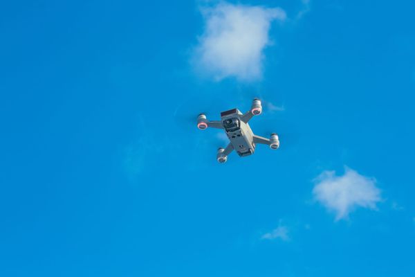 Aerial view of a drone cruising in a bright blue sky with scattered clouds by Pok Rie