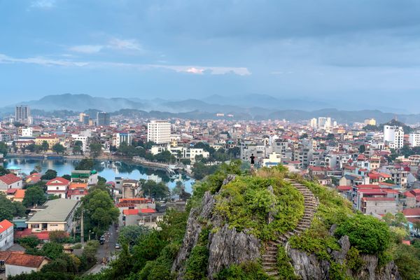Aerial view of Lang Son cityscape with lush green hill and distant mountains under a cloudy sky.
