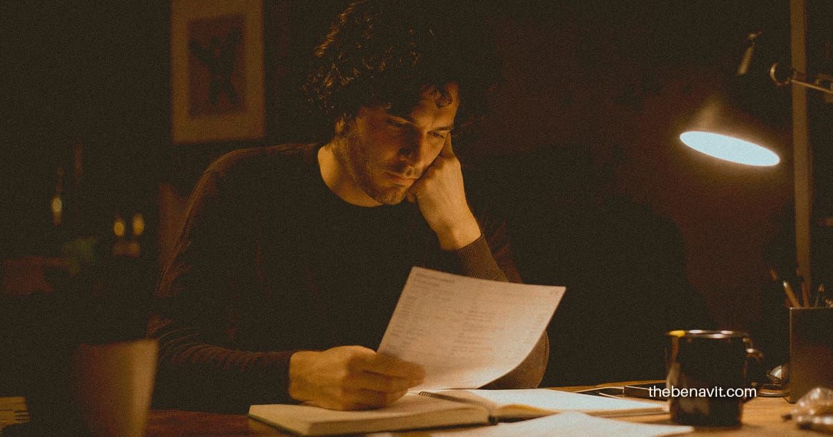 A person reviewing their finances at a desk in warm night light, looking thoughtful and reflective.