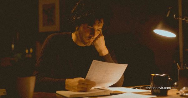 A person reviewing their finances at a desk in warm night light, looking thoughtful and reflective.