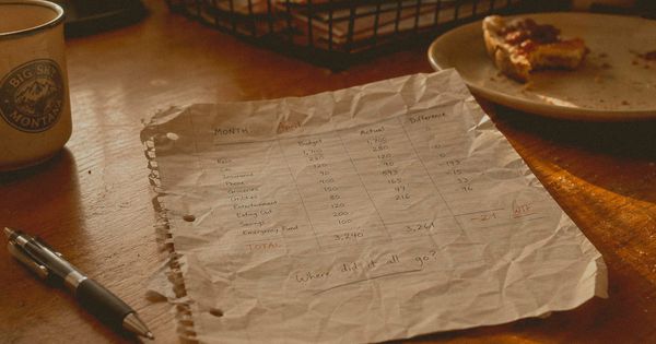 A crumpled budget notebook and thrown pen on a messy table, capturing the moment a financial plan gets abandoned.