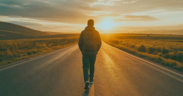 A person walking forward on an empty road at sunrise, capturing the quiet momentum of action that precedes motivation.