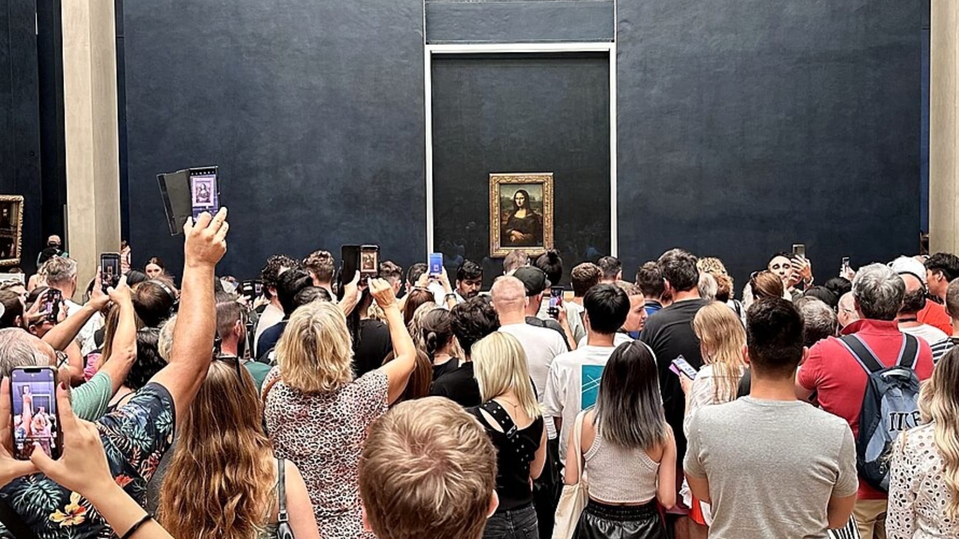 A crowd of people around the Mona Lisa, many taking photos using their smartphones.