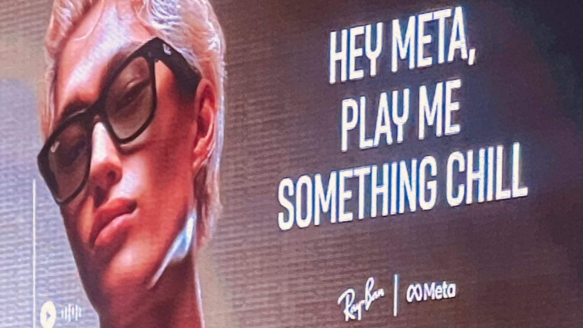 Snapshot of an electronic billboard advertising Ray-Ban smart glasses. It features a person wearing smart glasses and the message says: "Hey Meta, play me something chill". 