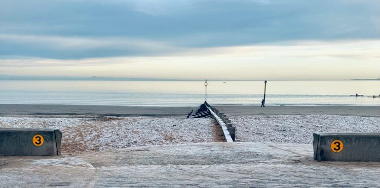 A view out to the sea from Portobello beach in Edinburgh on a winter's day - the sand is slightly frozen, and the groin stretches into a calm, sun-kissed bay