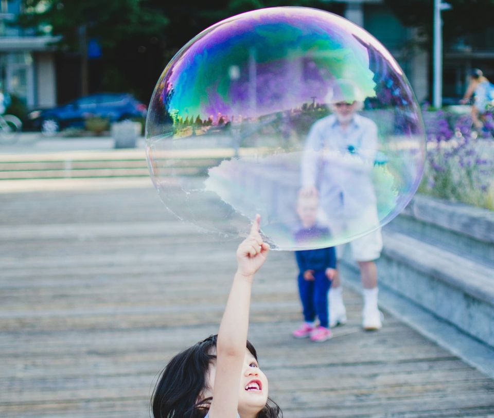 A young girl trying to pop a large bubble.