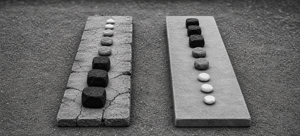 Black-and-white image of two parallel stone paths with the same stones in different orders; the heavy-stone-first path is cracked while the lighter-stone-first path remains smooth.