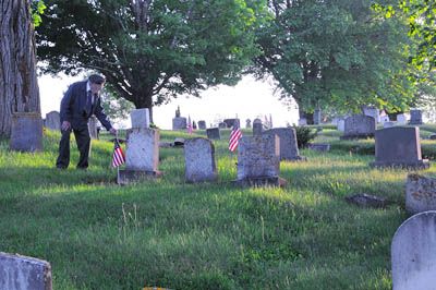 WORLD WAR II veteran Ed Browne of Dennysville pays respects to fellow veterans as he places a flag at a grave in the Dennysville Cemetery, in preparation for Memorial Day observances. (Edwar