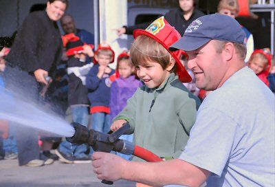 A FUTURE FIREFIGHTER? Firefighter Tom Critchley and kindergartner Jesse Calame try out spraying water with a fire hose during a visit to the Timothy P. Mullen Central Fire Station by Eastpor