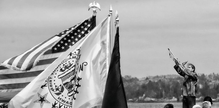 OFFERING PRAYERS with the peace pipe to the four directions is Darrell Newell, vice chief at Indian Township, at Split Rock, Sipayik. In the foreground, the Passamaquoddy Tribe's flag is fla