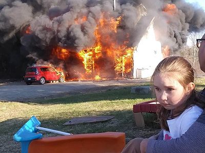 FIRE DESTROYS THE PERRY HOME of Larry and Tiffany Hilderbrand, as one of their daughters watches. (Photo courtesy of Larry Hilderbrand via Facebook)