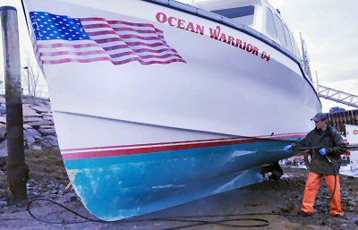 A SPRING RITUAL. Howard Calder cleans off the bottom of the Ocean Warrior, David Pottle's lobster boat, at the inner basin of the Eastport breakwater on a recent spring day. (Edward French p