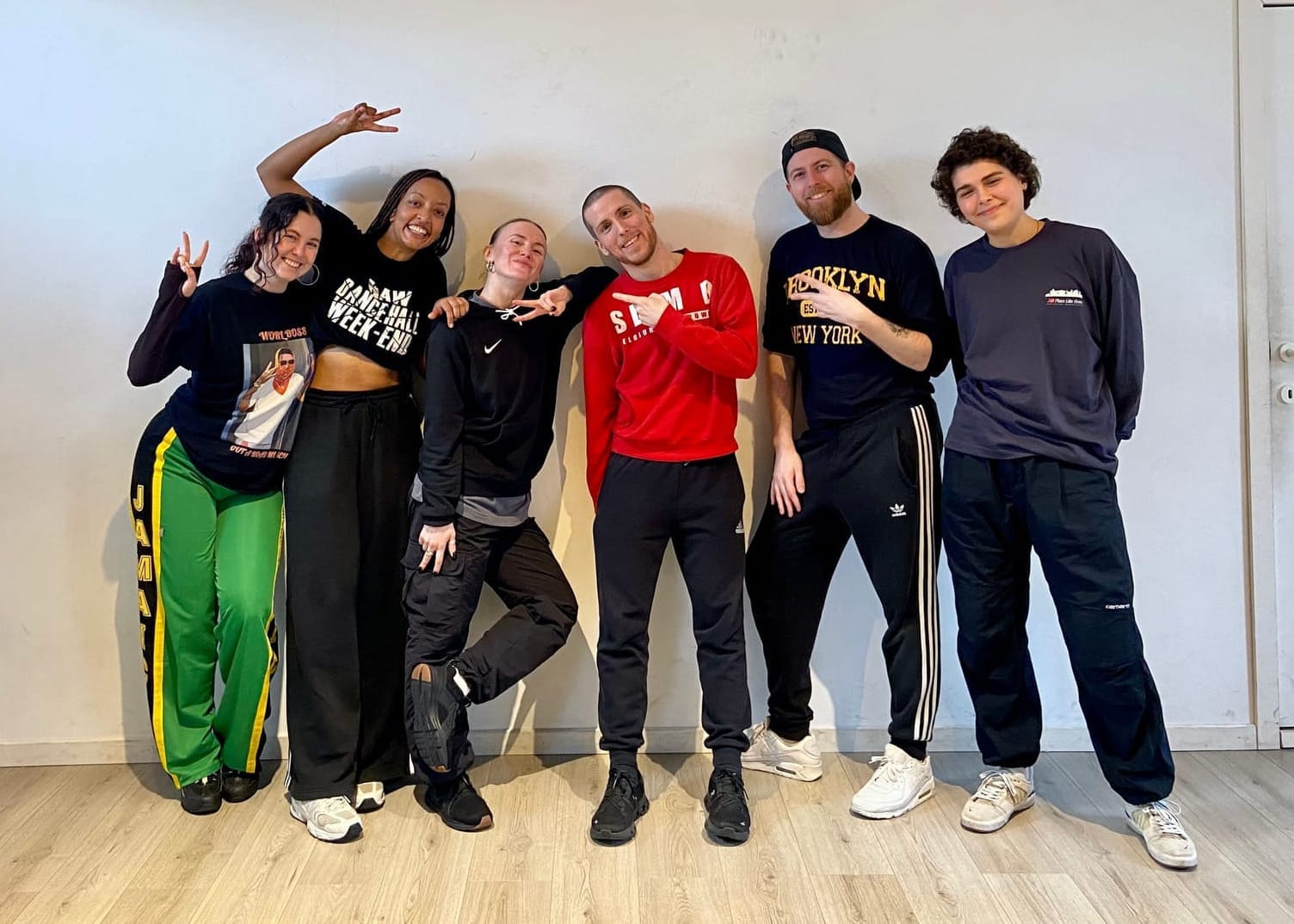 6 people leaning against white wall, looking at the camera. Di and SLim B are in the middle.