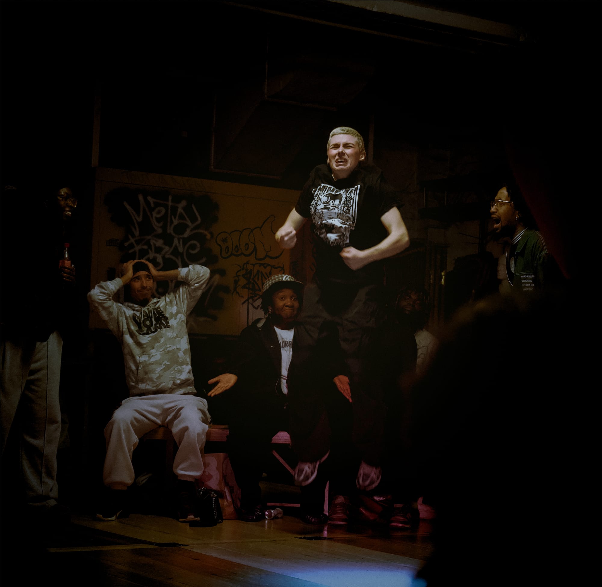 Baby P. Drickx is dancing Krump. She jumps in the air. The people behind her look in awe at her.