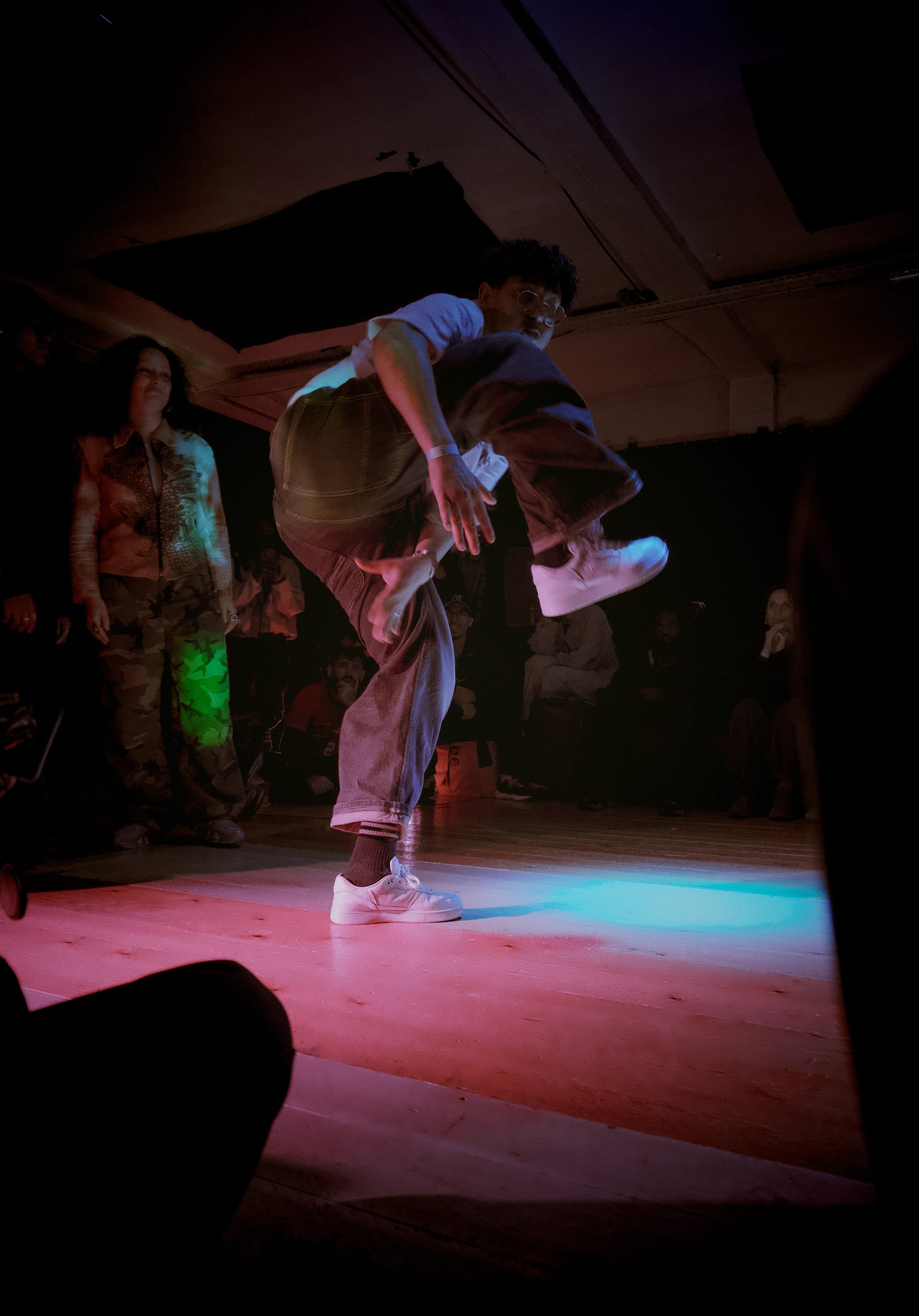 Dancer lifts his right leg and puts his left hand underneath that leg.