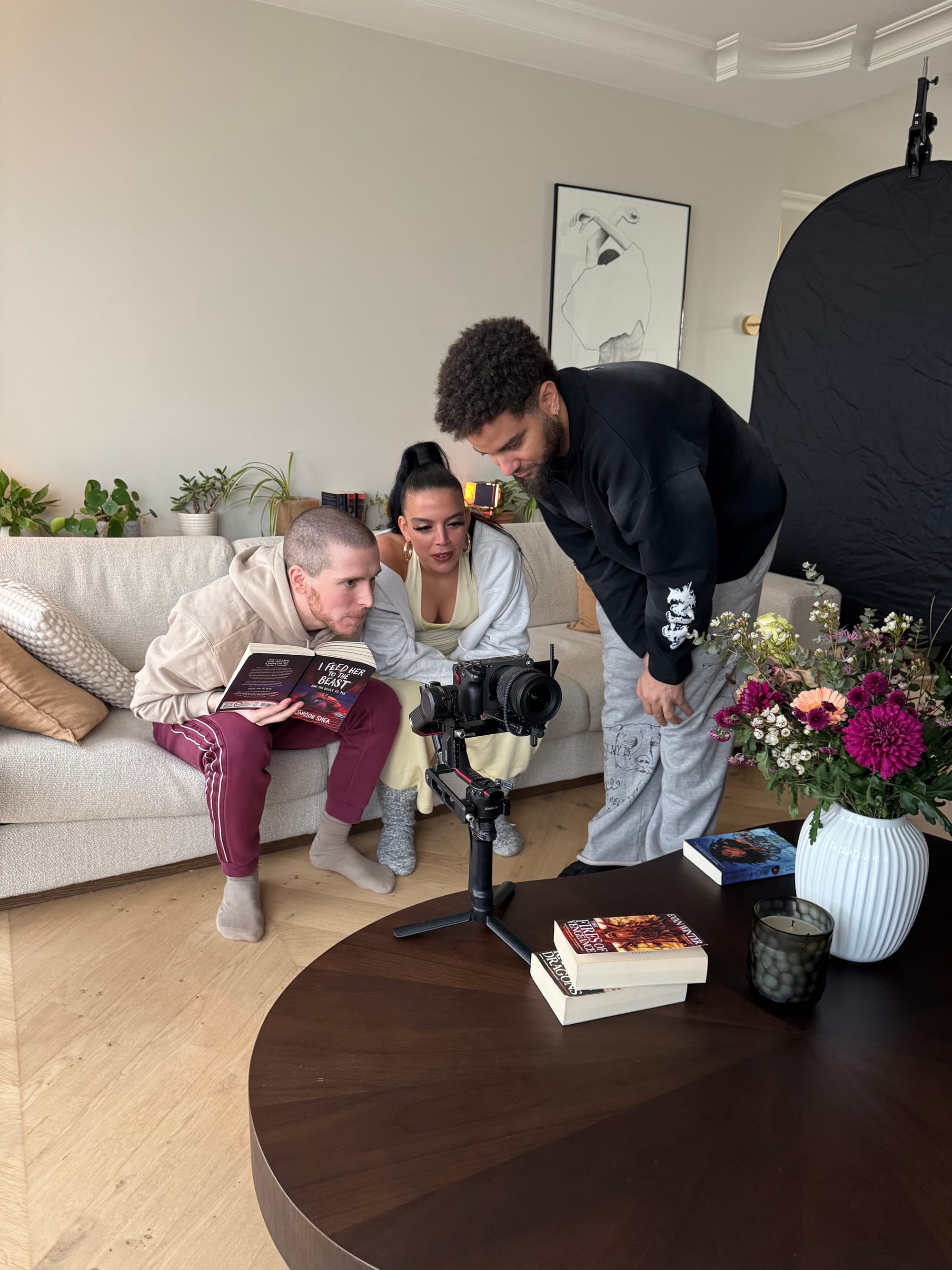 Slim B (sitting on the couch), Pippa (sitting on the couch) Adam (standing) are wathcing a take on the camera.