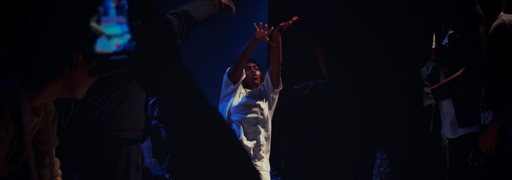 Kassy is dancing during the exhibition 5 vs 5 battle. She is surrounded by the other dancers and the audience.