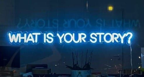 Window into an office with a neon sign that reads "What is your story?"