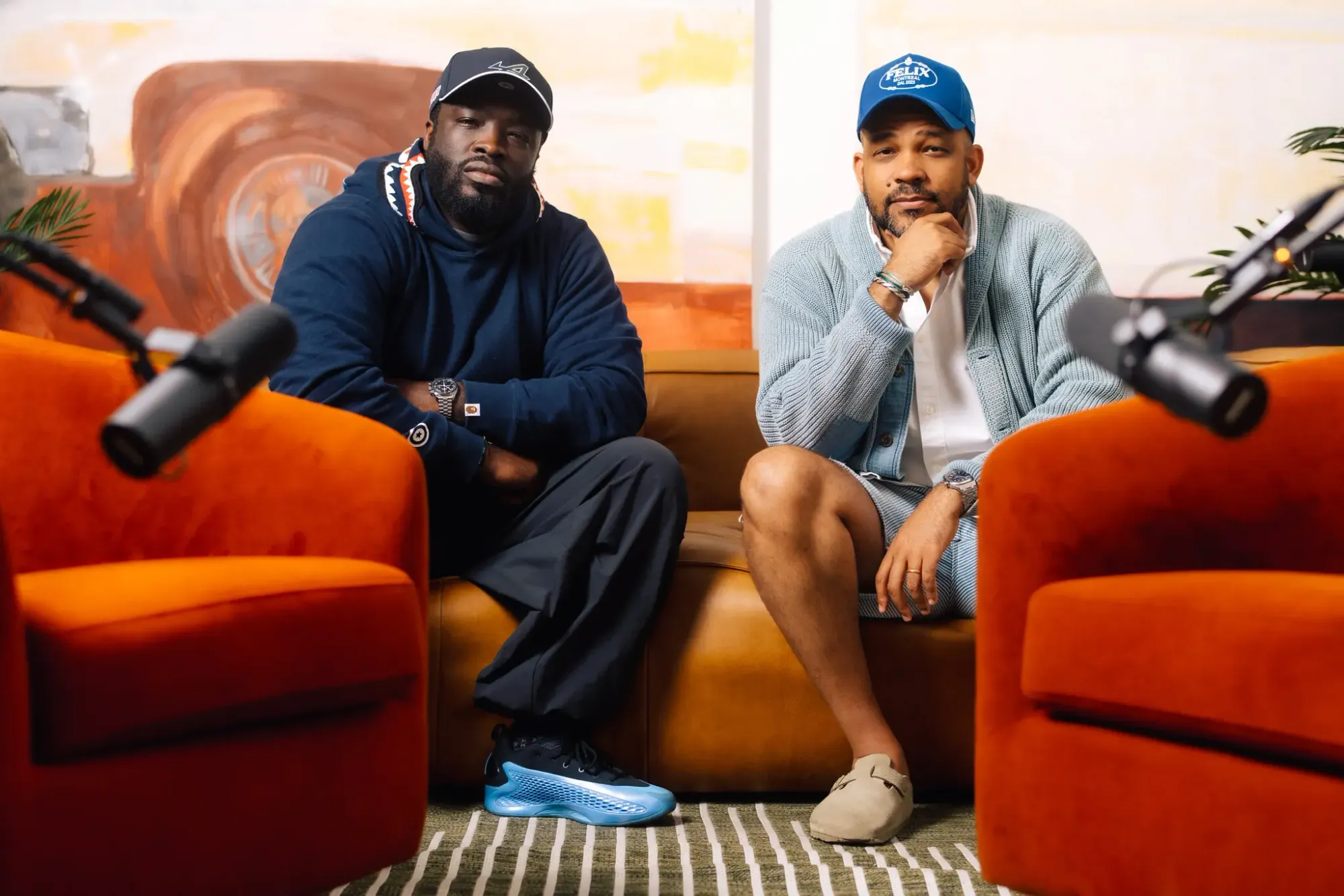 Two hosts sit between orange armchairs in a warm studio setup, microphones in frame. Perri Dash and Rashawn Smith of the Wrist Check Podcast, captured mid-conversation about watches, style, and culture.