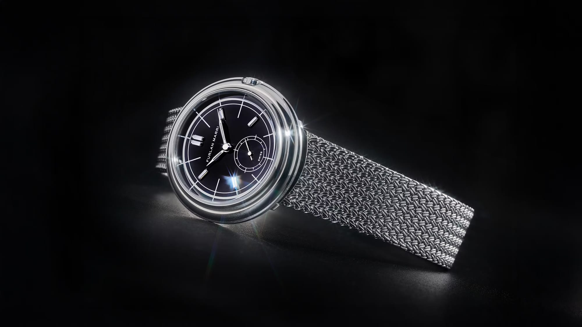Black dial Furlan Marri wristwatch with a polished case and woven metal bracelet, photographed against a dark background to highlight its sleek modern design.