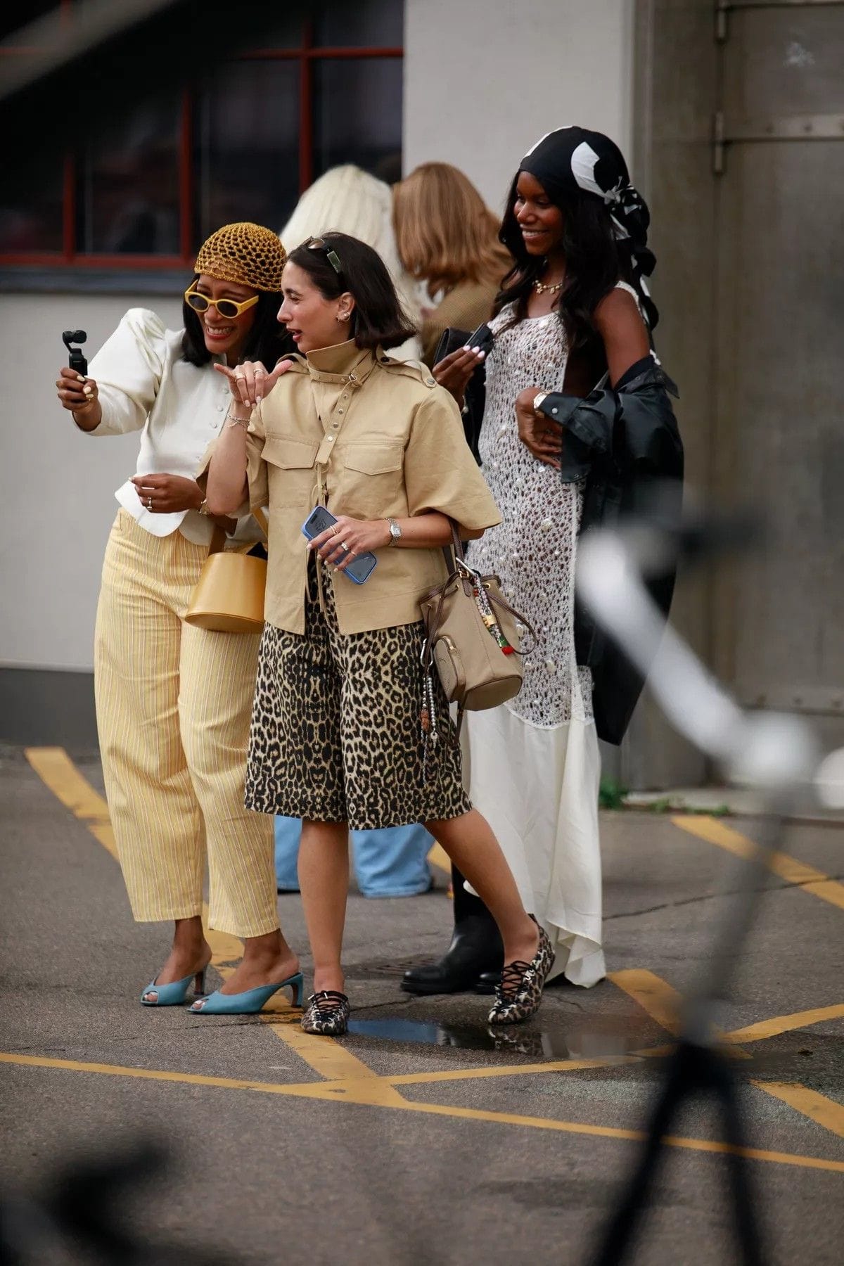 Group of stylish women taking a street-style selfie , wearing patterned and neutral tones with confident, modern flair.