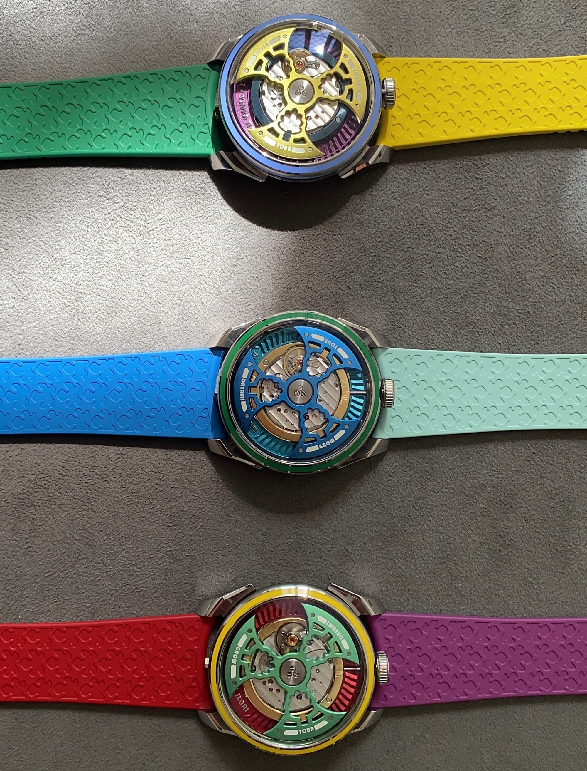 Three colorful mechanical watches from the Grow Your Dreams collection displayed on a dark surface, each featuring open-worked dials and matching rubber straps.